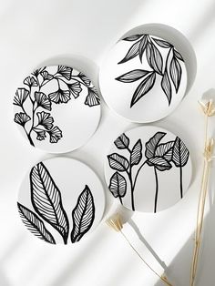 three plates with black and white designs on them sitting next to each other in front of a plant