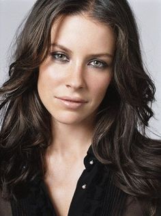 a woman with long brown hair wearing a black shirt and looking at the camera while posing for a photo