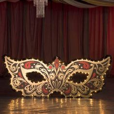 a masquerade mask sitting on top of a wooden floor next to a red curtain