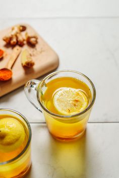 two glasses filled with lemon tea next to a cutting board