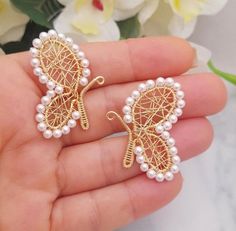 two pieces of gold and white pearls in the shape of butterfly brooches on a person's hand