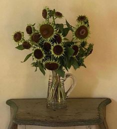 a vase filled with lots of sunflowers on top of a wooden table next to a wall