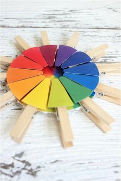 a rainbow colored wheel with wooden sticks sticking out of it on a white wood background