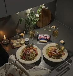 two plates of spaghetti on a table with candles and flowers in vases next to them