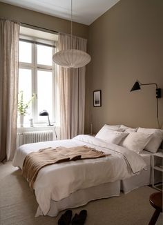 a bed sitting next to a window in a bedroom under a light fixture and a lamp