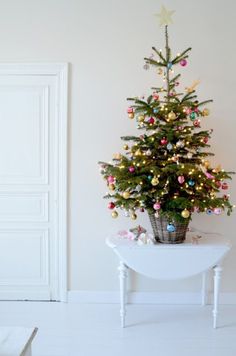 a small christmas tree sitting on top of a white table next to a wall with the words join me for christmas shopping