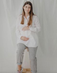 a pregnant woman sitting on a stool with her arms crossed and legs crossed, in front of a white backdrop