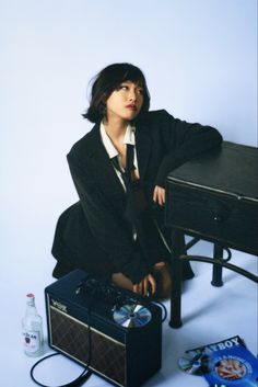 a woman sitting on the ground next to an old suitcase and record player in front of her