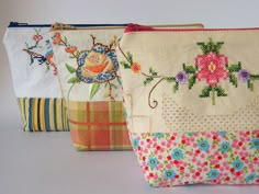 three small purses are lined up on a white surface, one is decorated with flowers and the other has an embroidered design