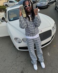 a man sitting on the hood of a white car holding money in front of his face