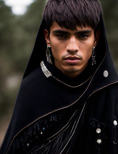 a young man wearing a black cloak and earrings