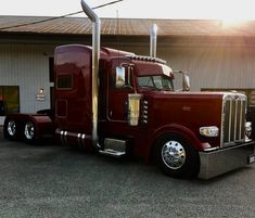 a large red semi truck parked in front of a building with the sun shining on it's side