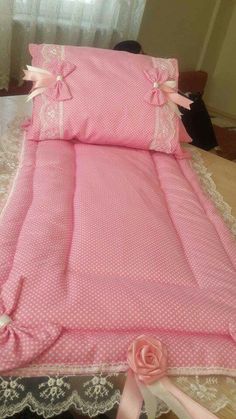 a pink bed with white lace and bows on the bottom, sitting on a table next to a window