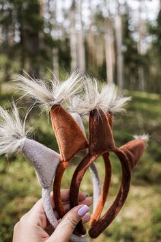 a person holding two brown and white hair accessories in their hands with trees in the background