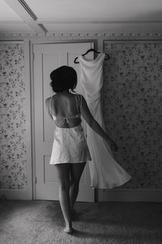 a woman standing in front of a dress on a hanger and looking at it