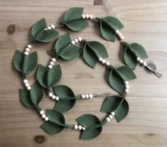 a necklace made out of green leaves and white beads on a wooden table with a tassel