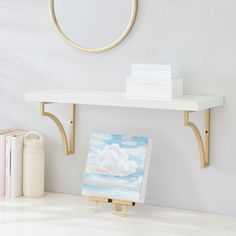 an easel with a painting on it next to a white wall and a round mirror