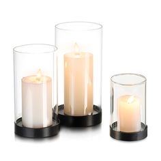 three lit candles in glass containers on a white surface with black rims and metal stand