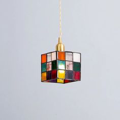 a multicolored light hanging from a gold colored cord on a gray wall background