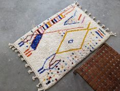 a white rug with multicolored designs on the floor next to a brick wall