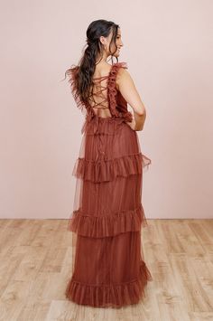 a woman in a brown dress standing on a wooden floor with her back to the camera