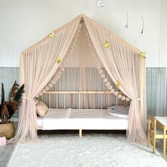 a canopy bed with sheer curtains and pillows on the floor next to a white rug