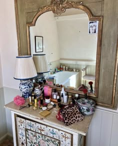 a dresser with an ornate mirror, lamp and other items on it in front of a bathtub