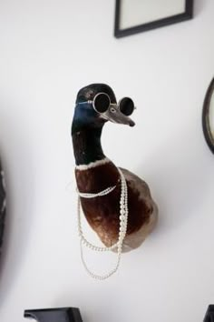 a duck with pearls on it's neck hanging from the wall next to two clocks