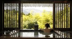 a woman is sitting in the jacuzzi looking out at the mountains and trees