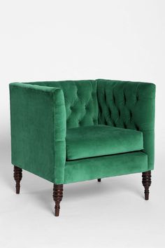 a green velvet chair with wooden legs and buttons on the arm rests against a white background