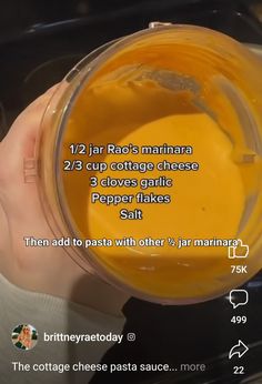 a person holding a blender filled with orange liquid and ingredients to make it into a smoothie