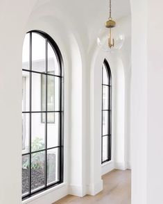 an empty room with arched windows and wood flooring is pictured in this image, there are two chandeliers hanging from the ceiling