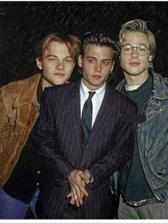 three young men standing next to each other in front of a rain soaked background with one man wearing a suit and tie