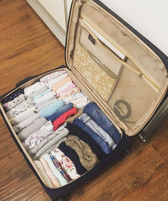 an open suitcase filled with clothes on top of a hard wood floor