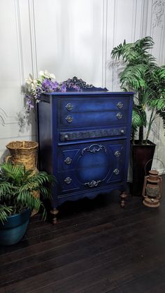 a blue dresser sitting on top of a wooden floor next to two potted plants