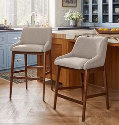 two stools in the middle of a kitchen with blue cabinets and counter tops on either side