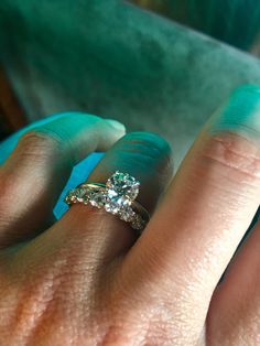 a woman's hand with a diamond ring on top of her finger and an aqua colored background