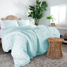 a bed with blue comforter and pillows in a room next to a potted plant