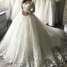 a woman standing in front of a window wearing a white wedding dress with long sleeves