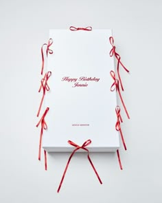 an open birthday card with red ribbon on the front and back of it, sitting on top of a white box