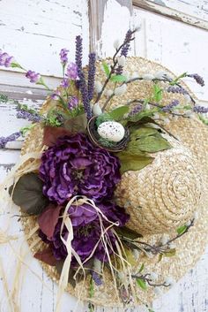 a straw hat with purple flowers and an easter egg on the top is hanging from a wall