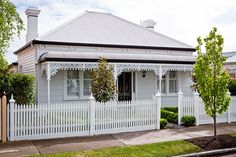 a white house with a picket fence and trees in the front yard on a sunny day