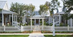 a white picket fence is in front of some small houses with trees and bushes around it