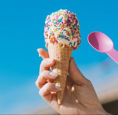 a hand holding an ice cream cone with sprinkles on it and blue sky in the background