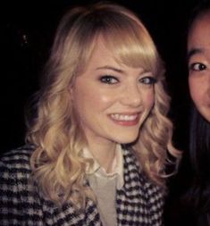 two beautiful young women standing next to each other in front of a dark background and smiling