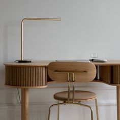 a desk with a chair and a table lamp on it in front of a white wall