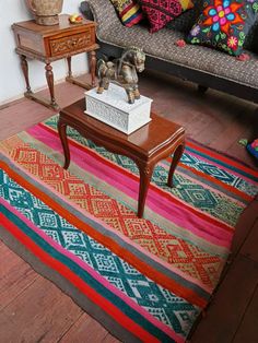 a living room with a couch, table and colorful rugs on the floor in front of it