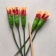 three green stems with red and yellow flowers next to chopsticks on a white surface