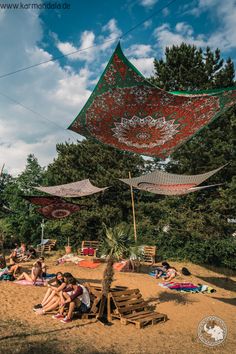 many people are sitting on the beach under some umbrellas and hammock nets