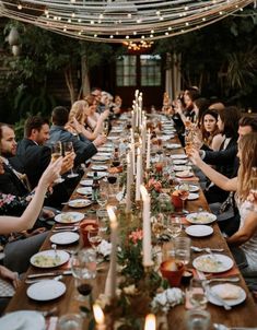 a group of people sitting at a long table with plates and wine glasses on it